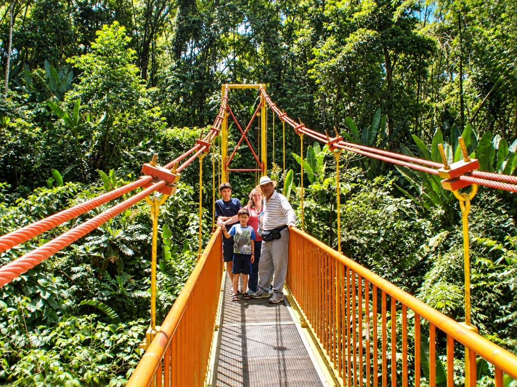 La familia con un guía en un puente colgante amarillo, entre la vegetación del Jardín Botánico