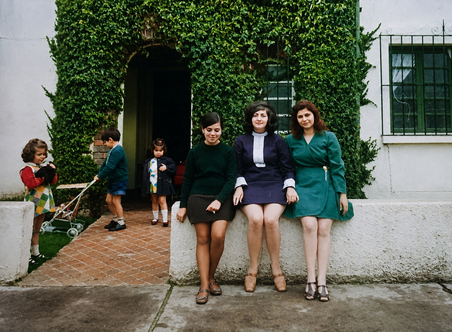 Fotografía de principios de los años 70: madre, tía y amiga sentadas en el muro del jardín, con minifaldas a la moda de la época
